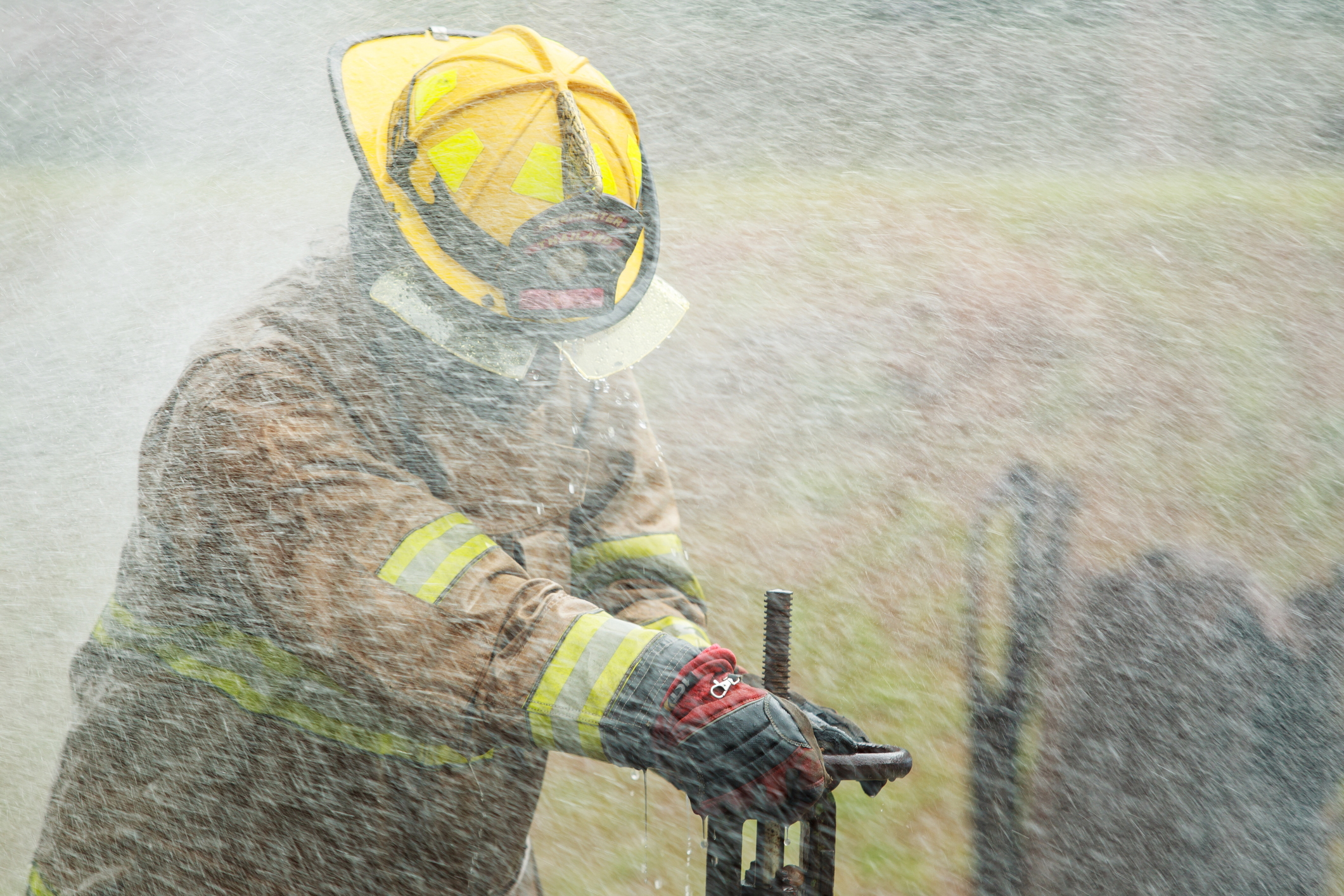 Close up action shot of firefighter's gloved hands operating a metal water valve during training. Amidst spray and smoke. Physical intensity and mechanical precision of fire suppression operations.