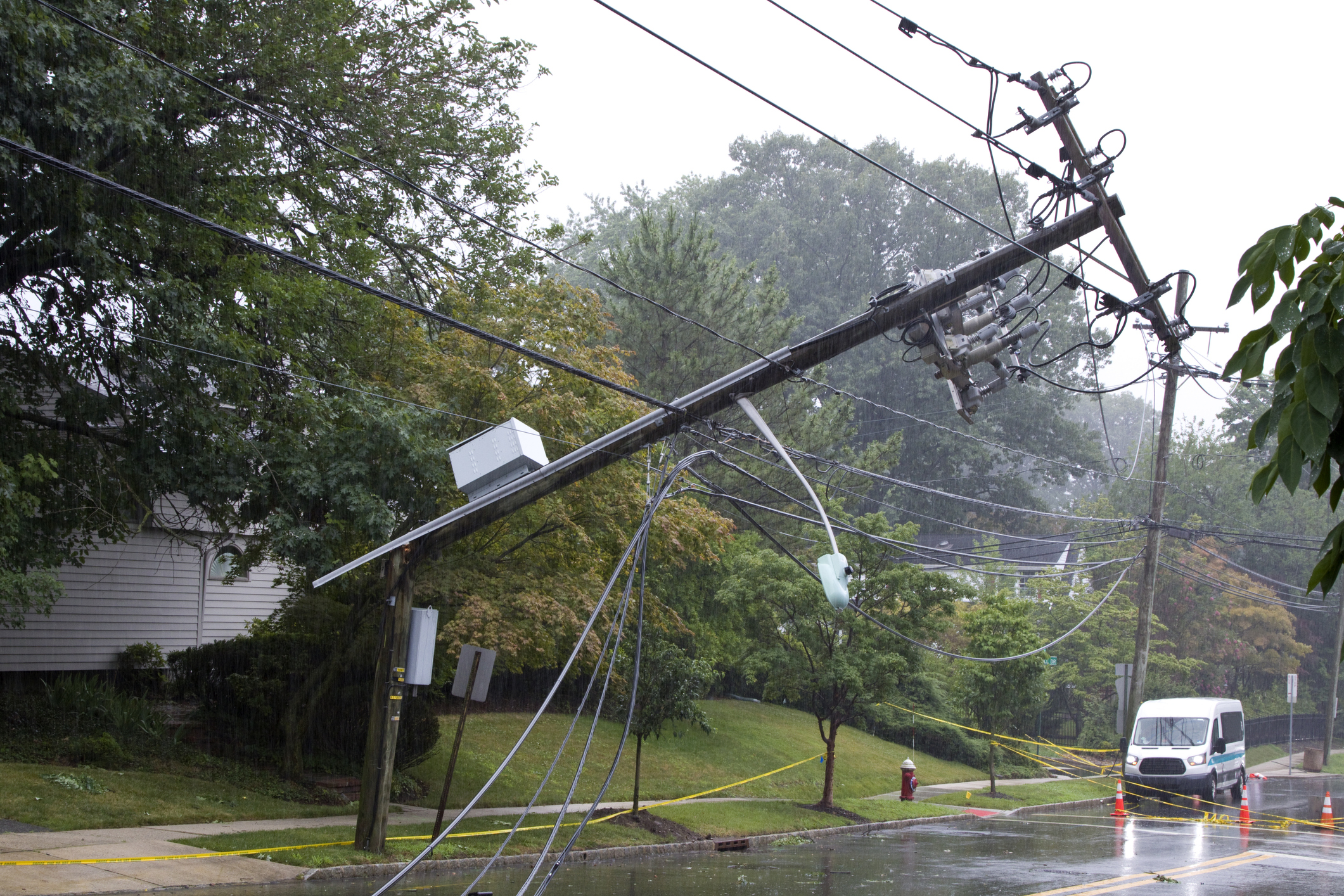 Storm damage with downed electrical pole and wires on residential street.